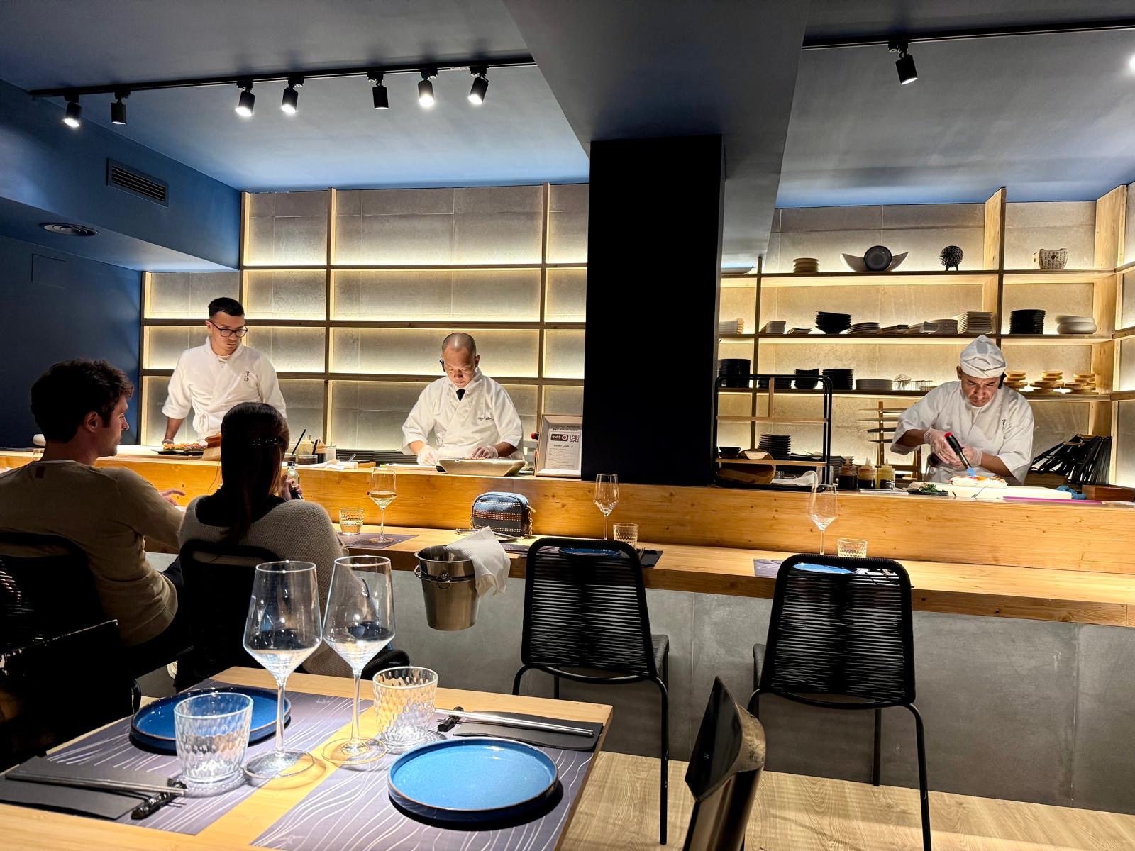 Tres cocineros trabajando tras la barra de sushi de madera clara
